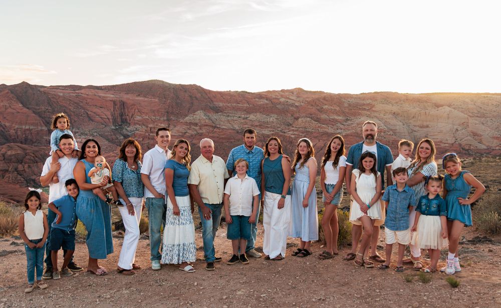Large family group portrait outdoors in desert canyon landscape at golden hour, wearing coordinated teal and white outfits.