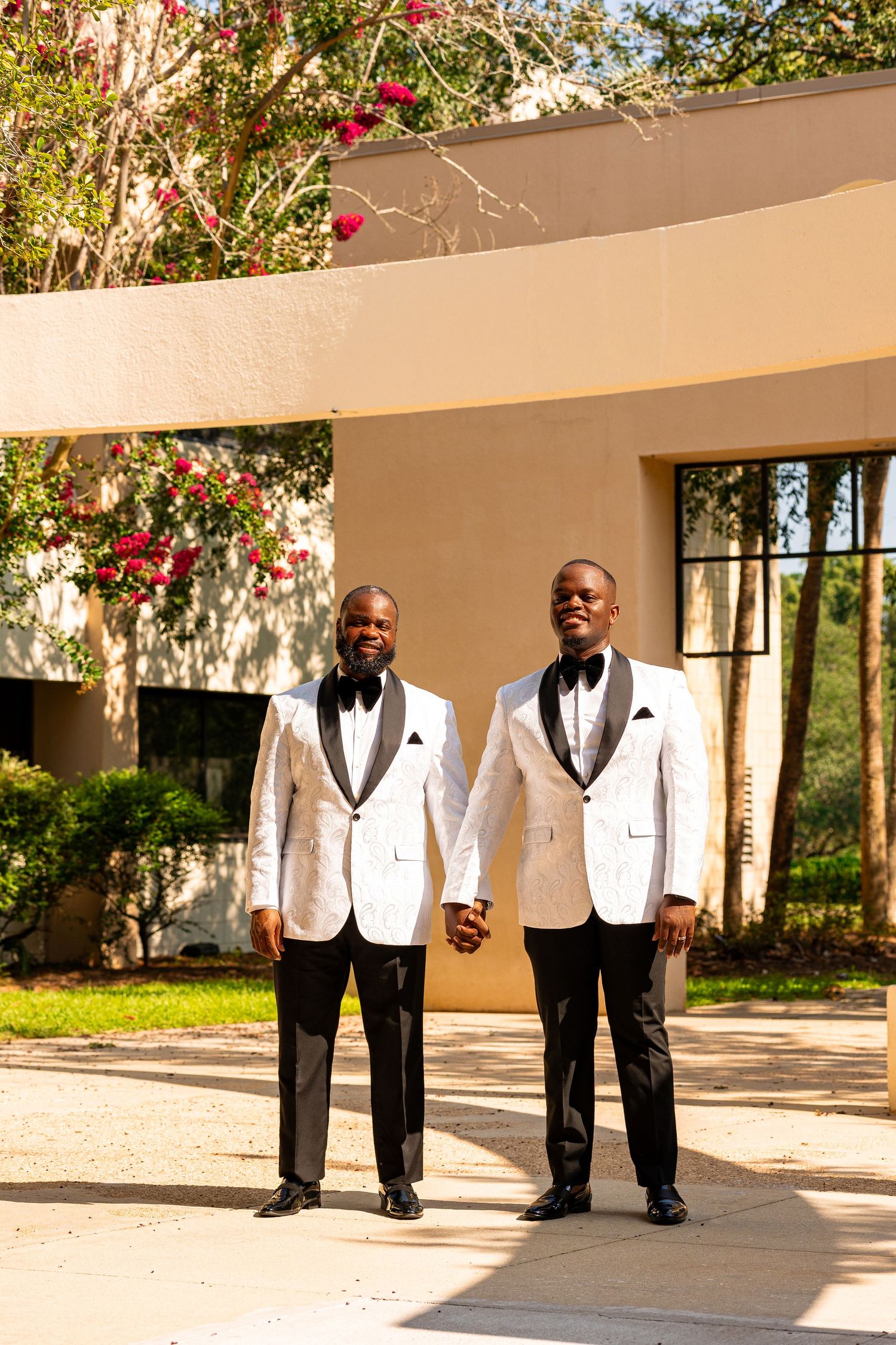 Two people in matching white tuxedo jackets and bowties pose elegantly outdoors. Engagement photographer. Wedding photographer.
