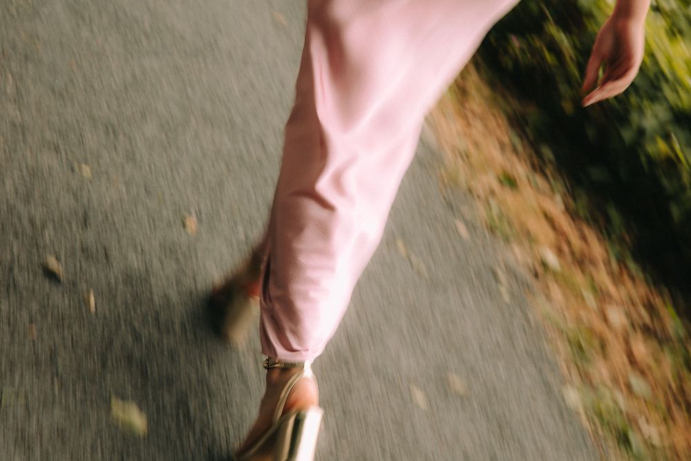 Close-up of a woman in a pink dress walking in gold heels on a path, with motion blur effect.