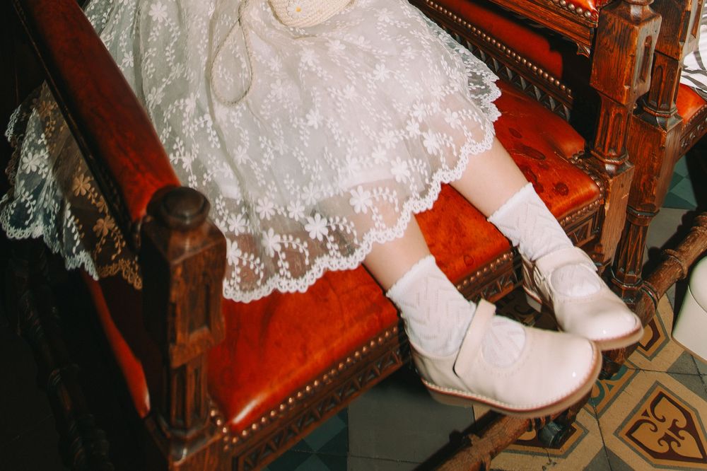 White lace dress with white ankle boots and socks on a child sitting on a red velvet chair.