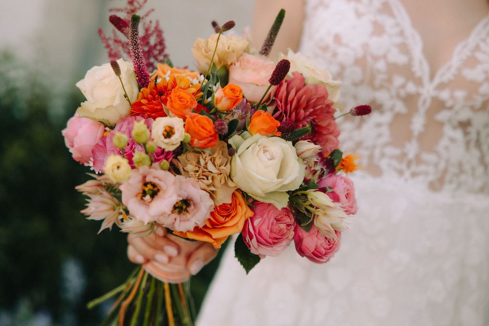 Bride holding a vibrant wedding bouquet with pink, orange, and white roses and mixed blooms in lush floral arrangement.