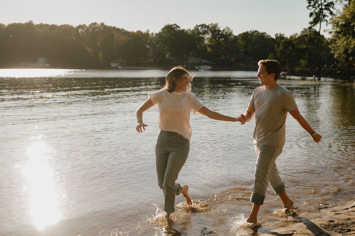 Couple splashing and playing together at sunset along the shoreline of a lake.