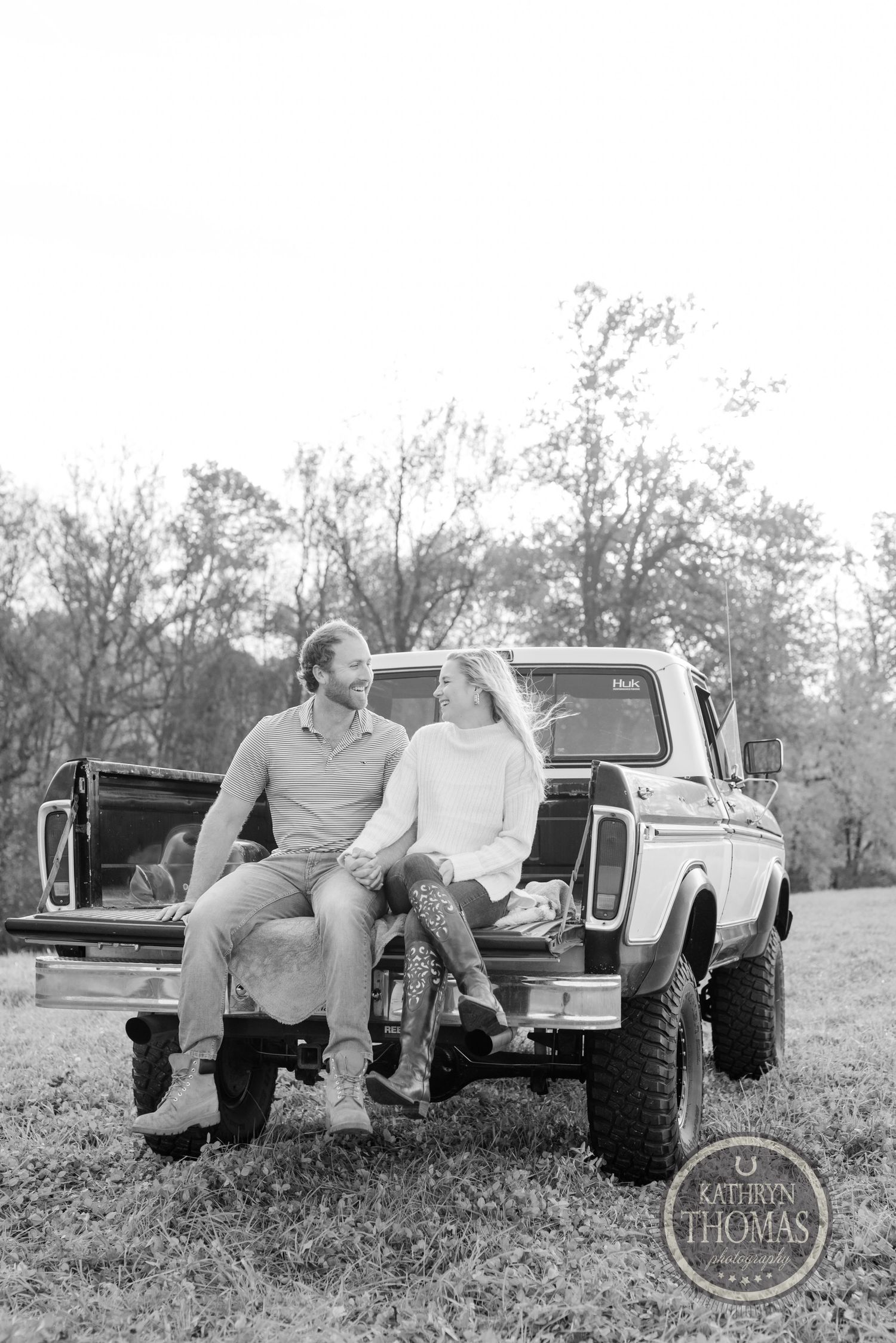 Black and white portrait of couple sitting on tailgate of vintage pickup truck.