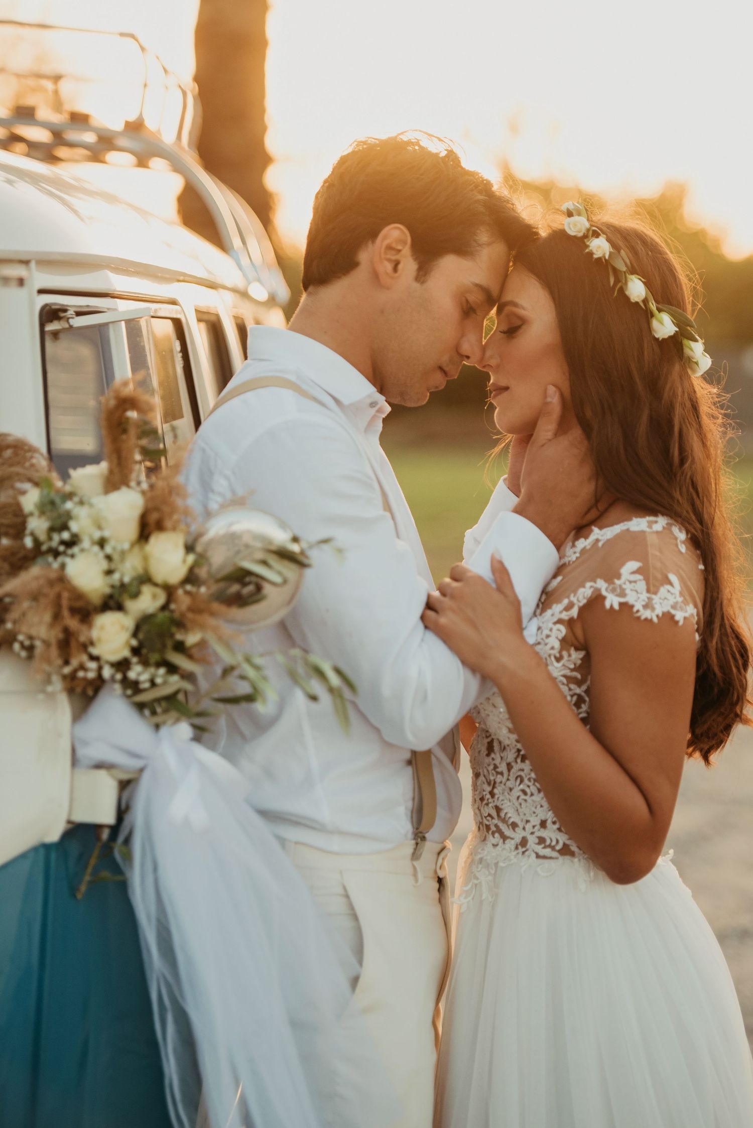 Romantic sunset portrait of couple embracing near vintage car with floral bouquet.