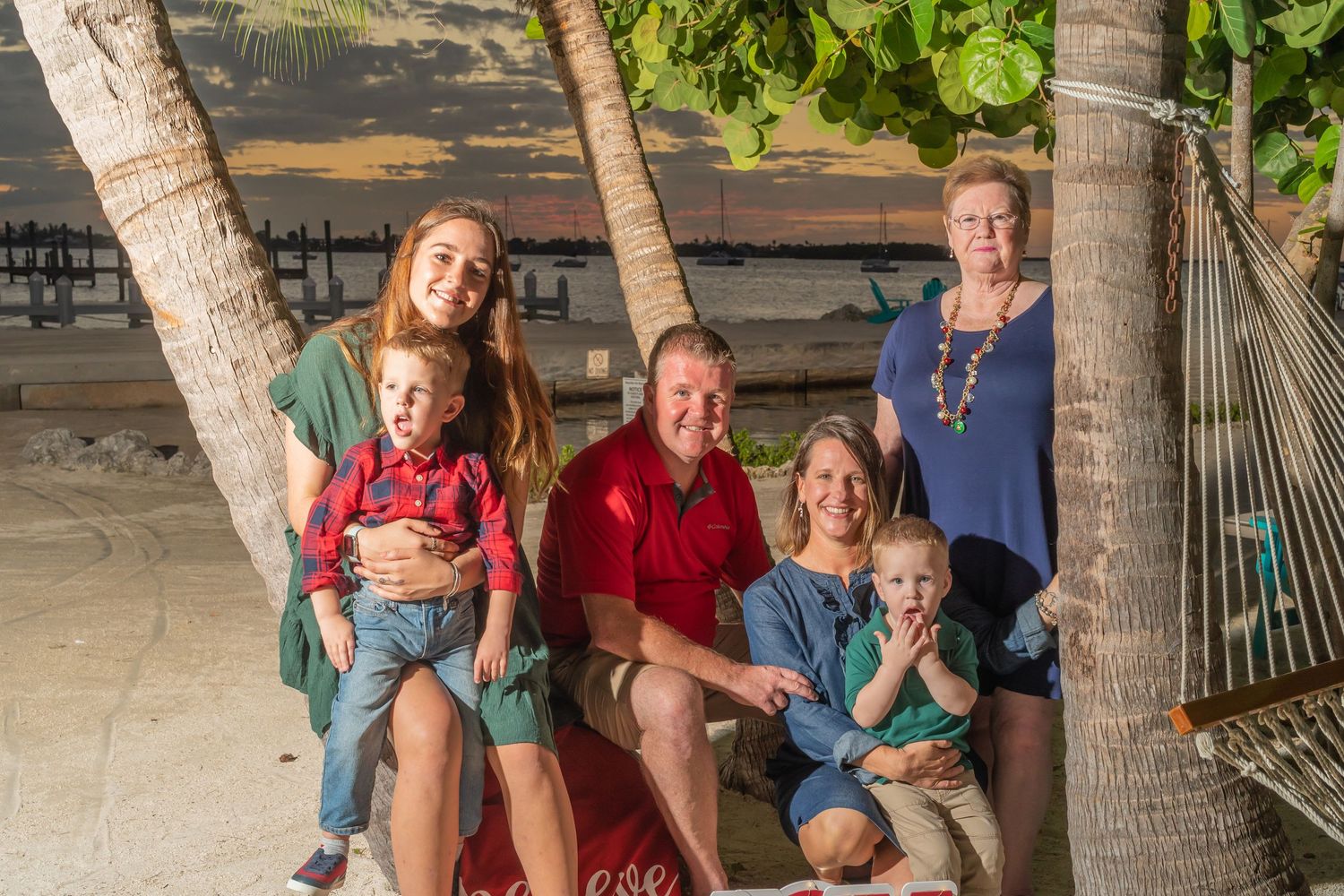 Family gathering under palm trees at night with holiday decorations.