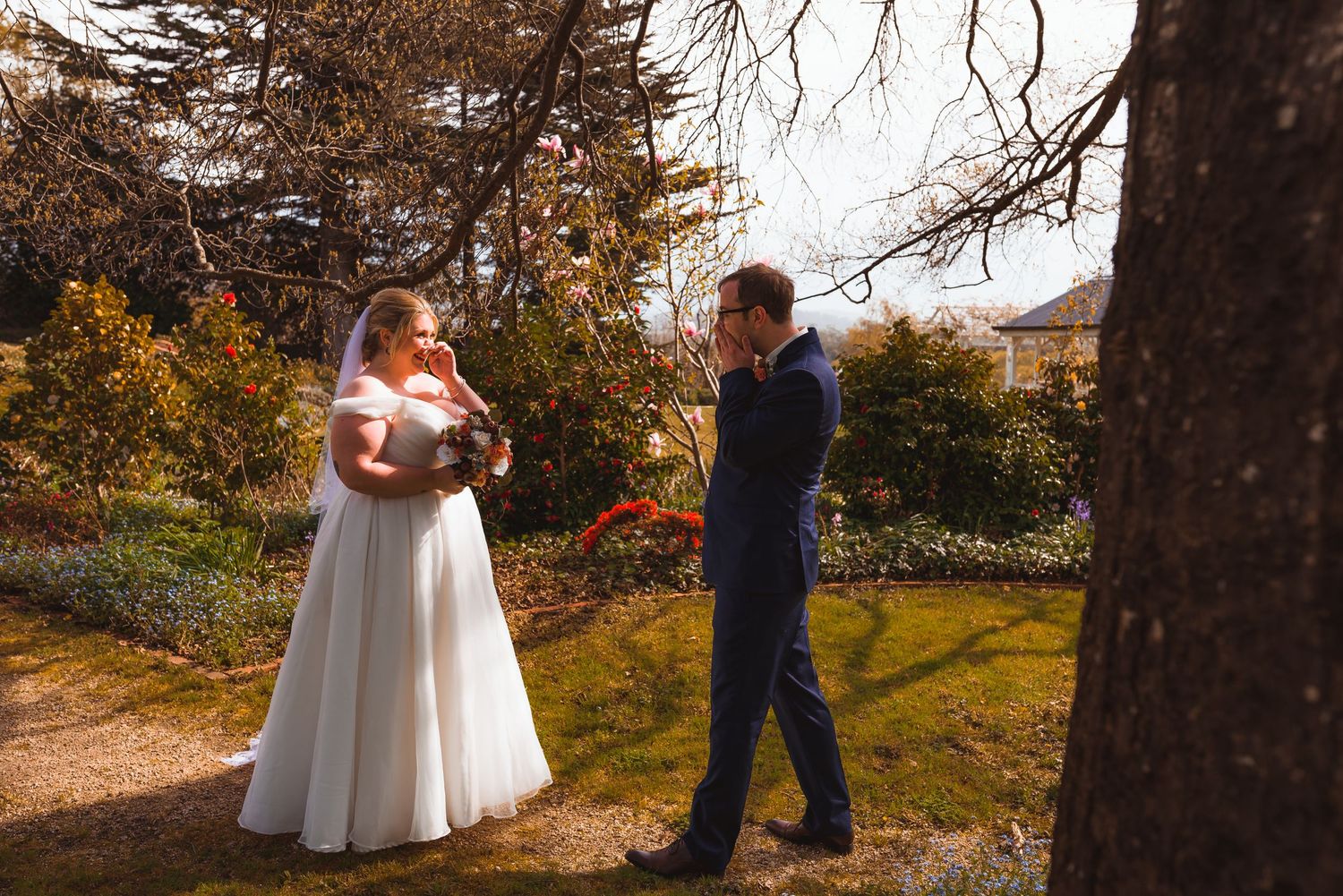 A couple in wedding attire stands on an autumn path surrounded by fall foliage.