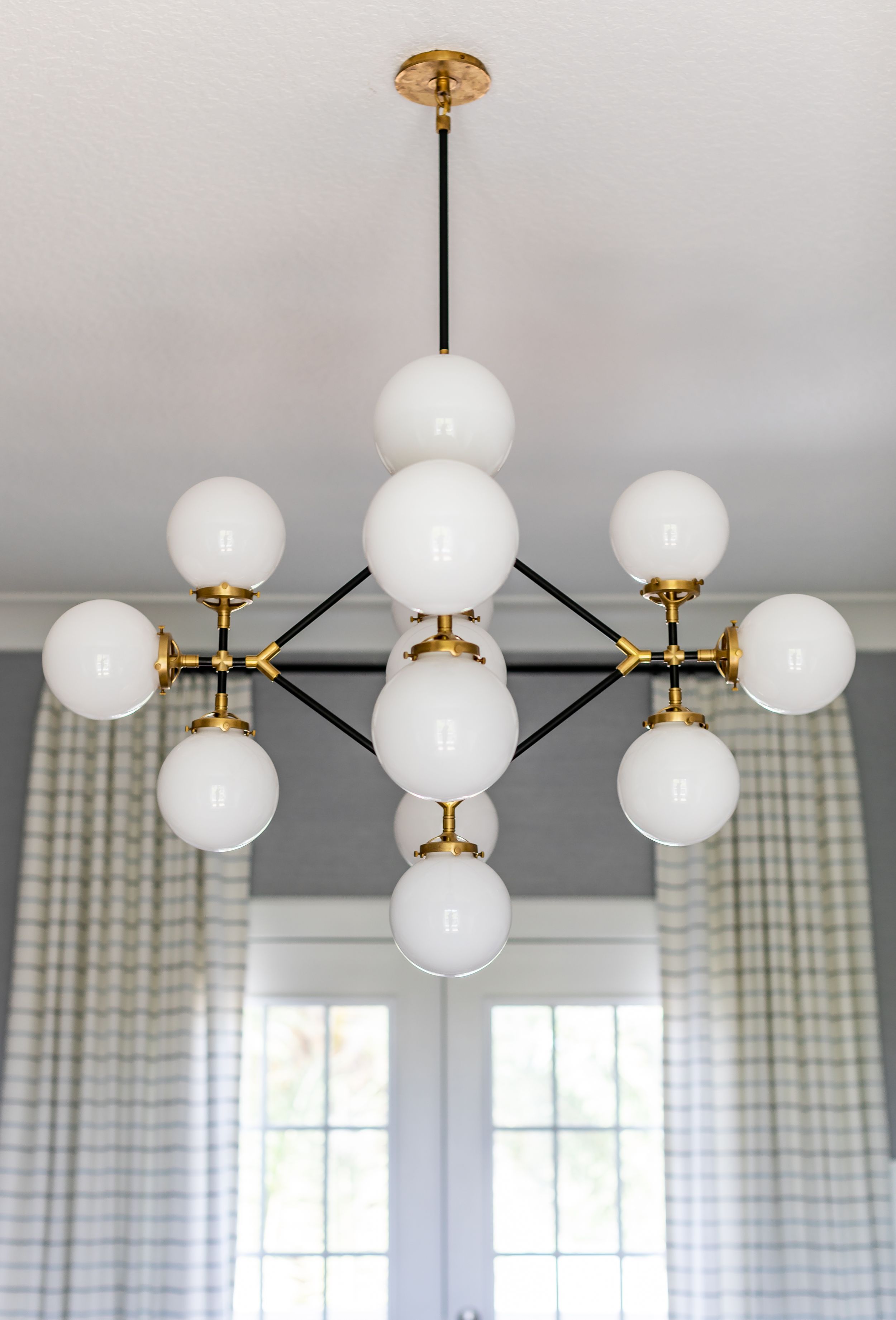Modern Visual Comfort chandelier against grey upholstered wall.