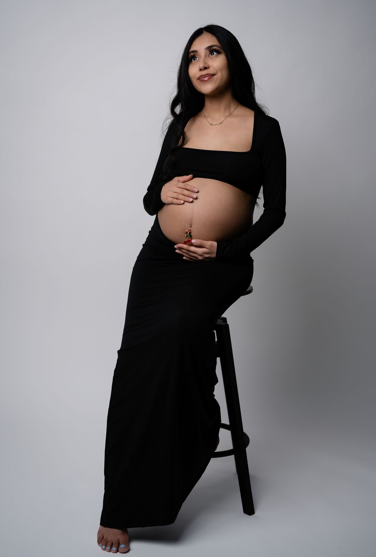 Minimalist maternity photoshoot with person wearing black against white backdrop.