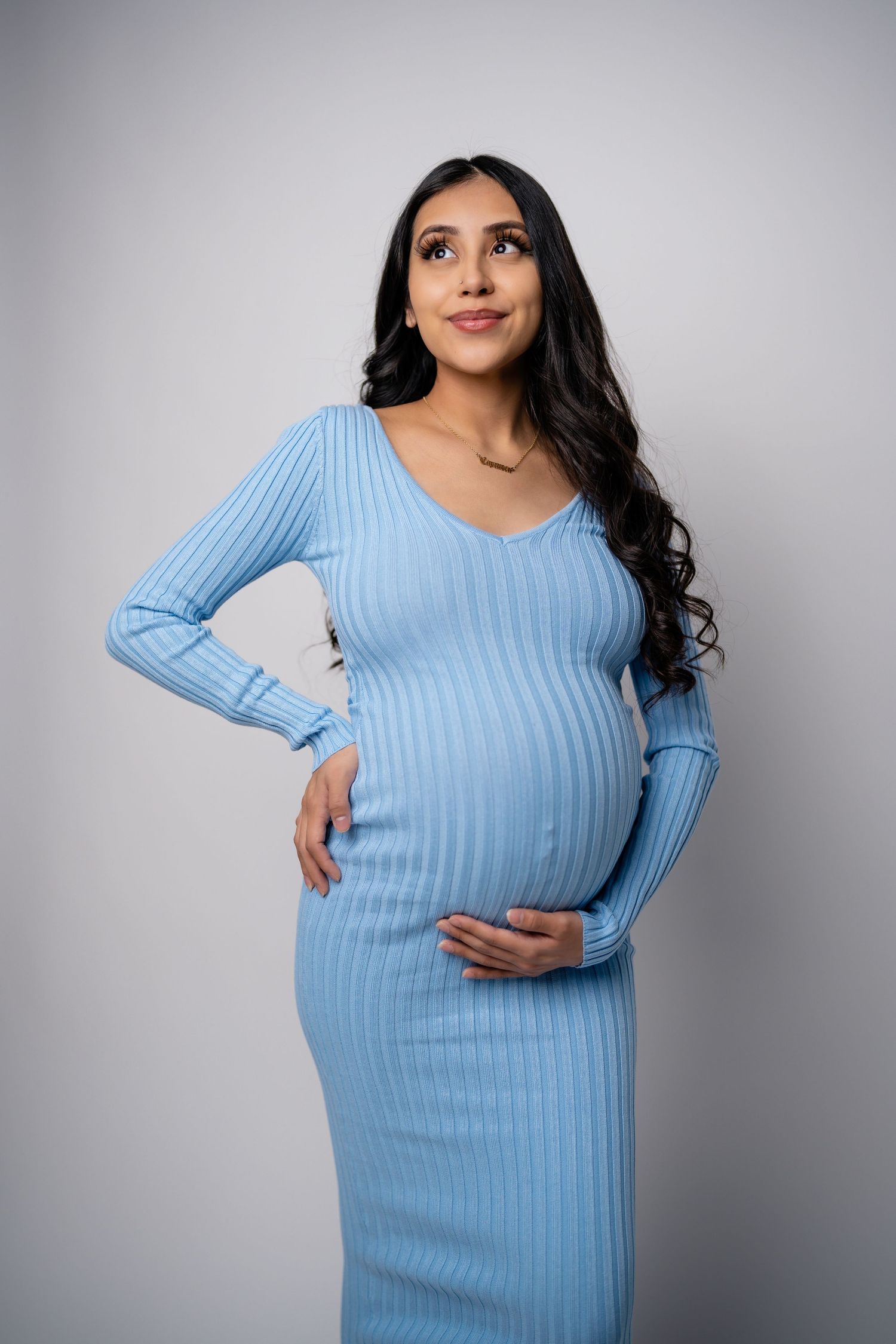 Maternity photos showing someone in a fitted light blue ribbed dress against white background.