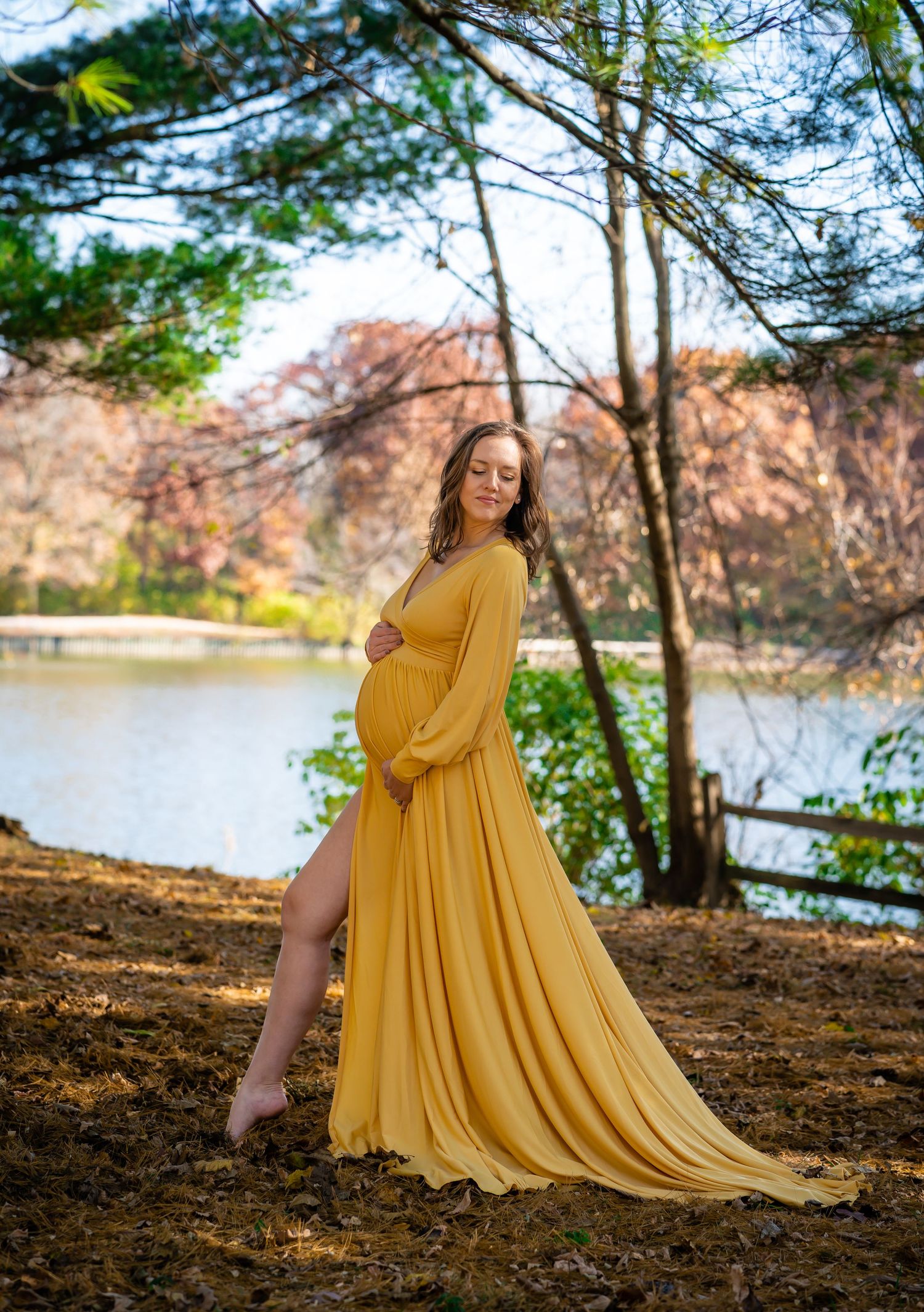 Flowing yellow dress maternity photoshoot in a natural forest setting near a lake.