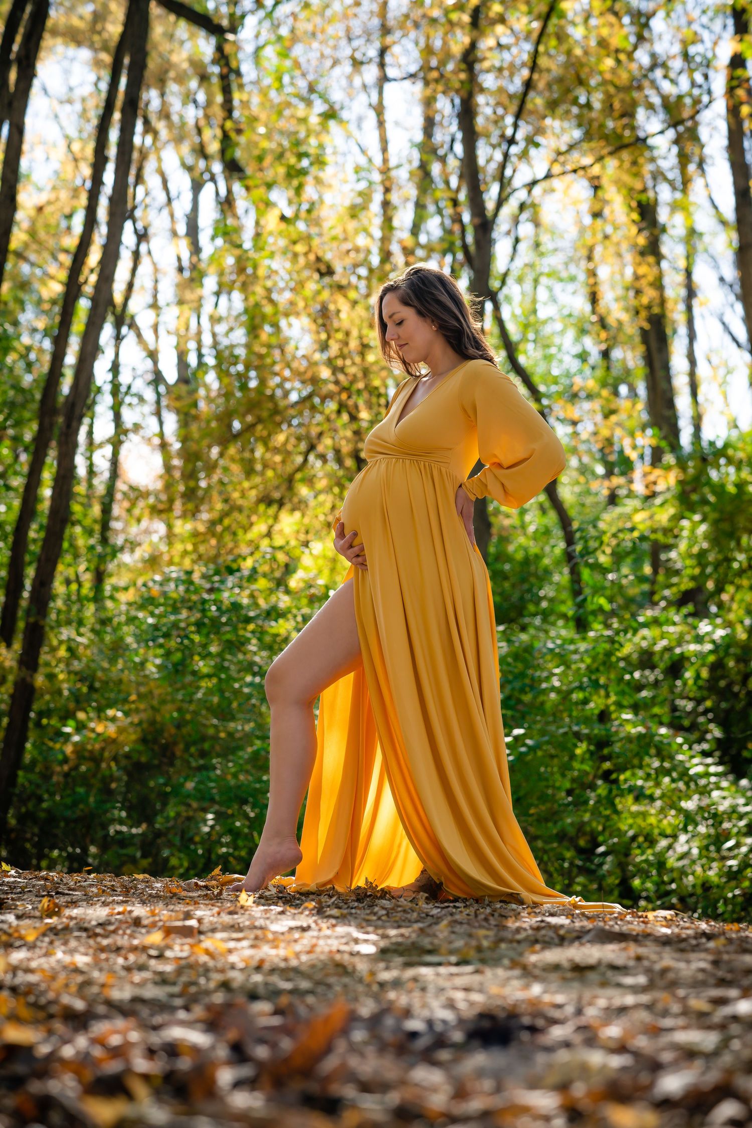 Maternity photo session in autumn forest with flowing yellow dress.