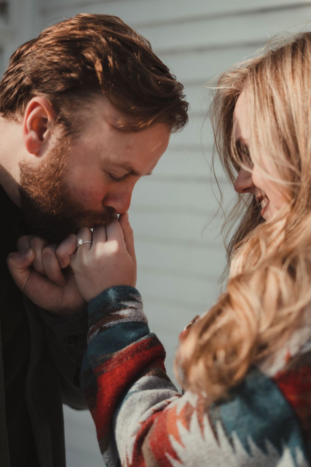 A tender moment captured as a couple embraces in soft lighting, with him gently kissing her hand.