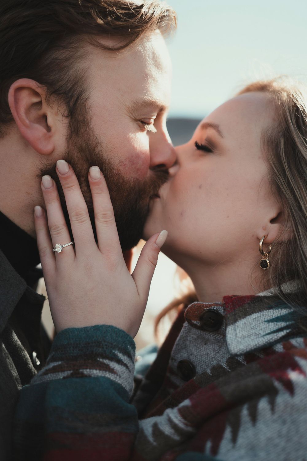 An intimate kiss shared between a couple wearing winter clothing against a bright background.