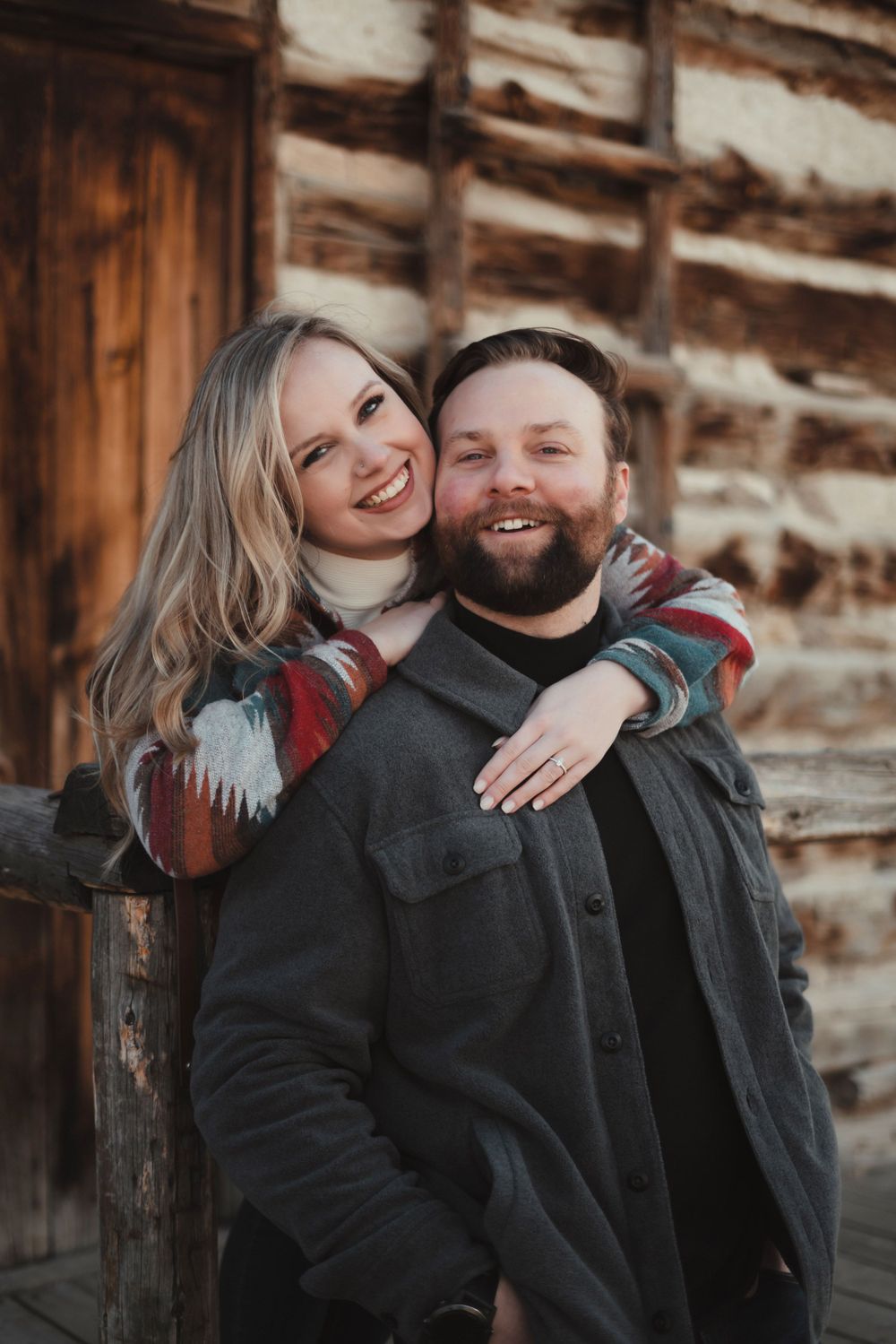 A joyful couple shares a loving embrace against a rustic wooden wall background.