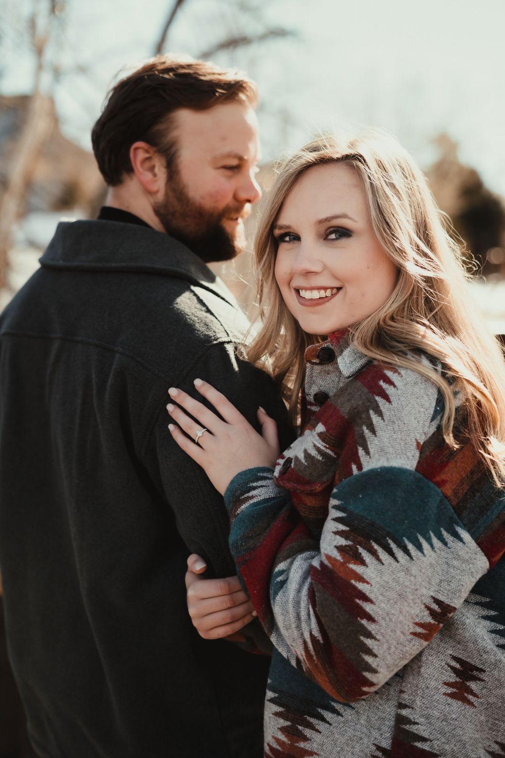 A couple in winter clothing shares a tender moment against a sunlit backdrop.