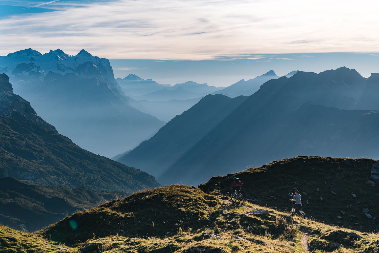 Mountain biker silhouetted against layered mountain ranges in golden evening light.