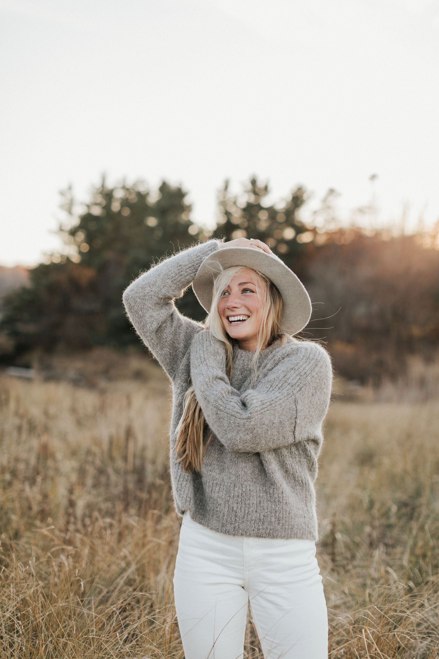 A cozy autumn scene with someone wearing a knit sweater and white pants in a golden field at sunset.