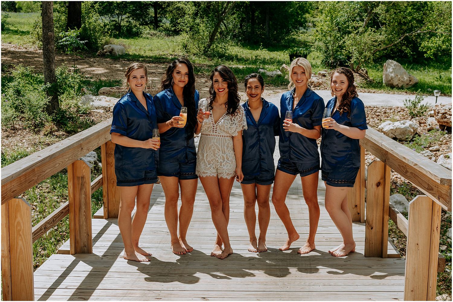 Wedding party in matching navy outfits poses together on wooden bridge outdoors.