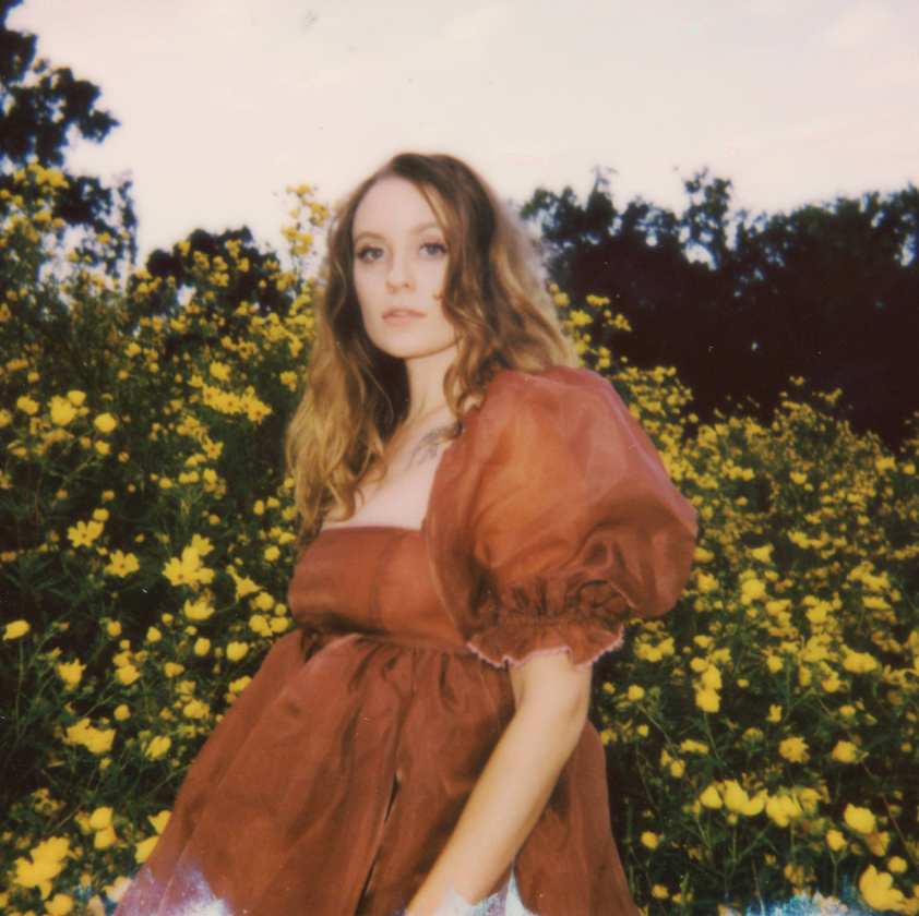 Portrait of woman in rustic brown dress against field of yellow wildflowers.