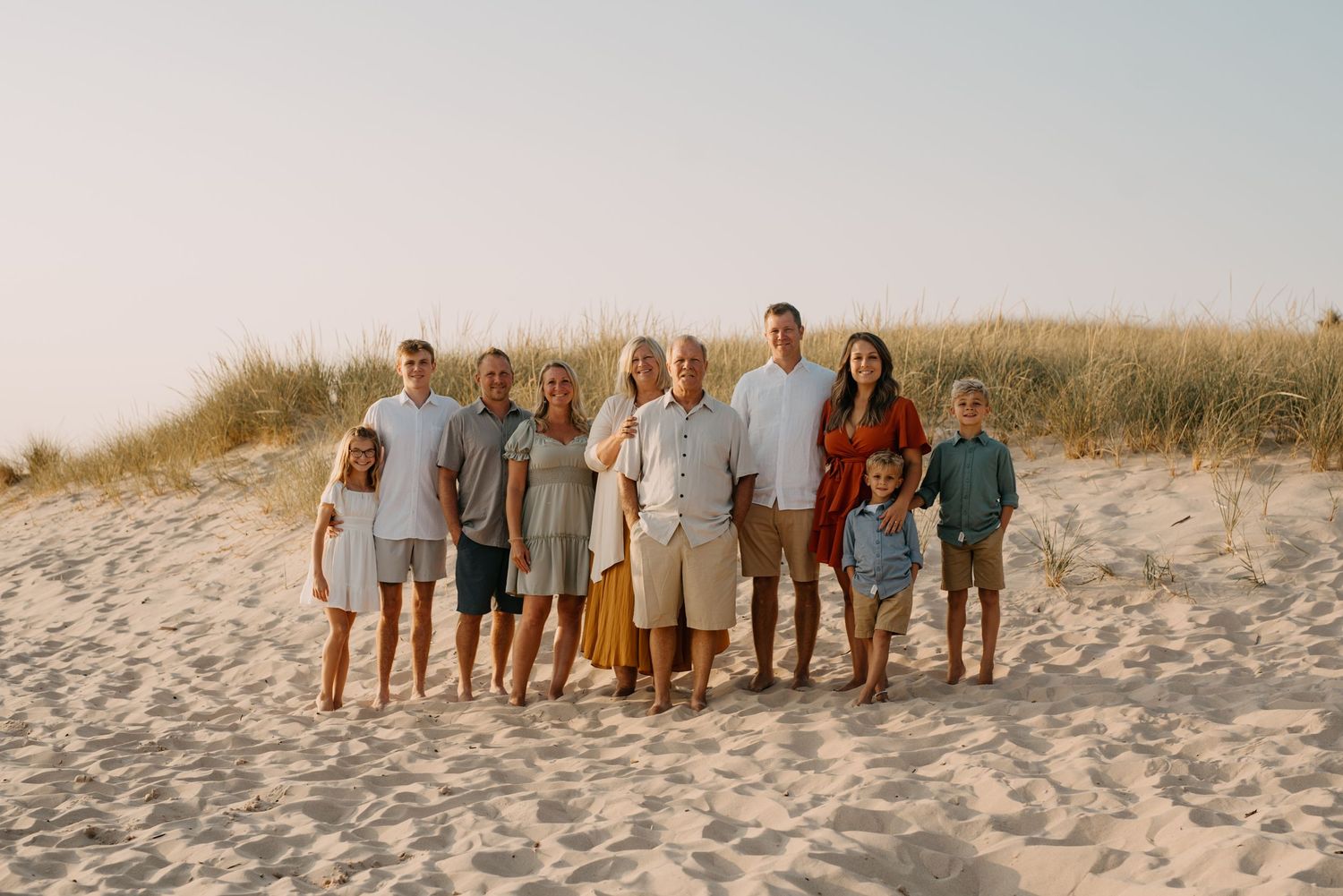 A group poses together on a sandy beach at sunset wearing coordinated light colored clothing.