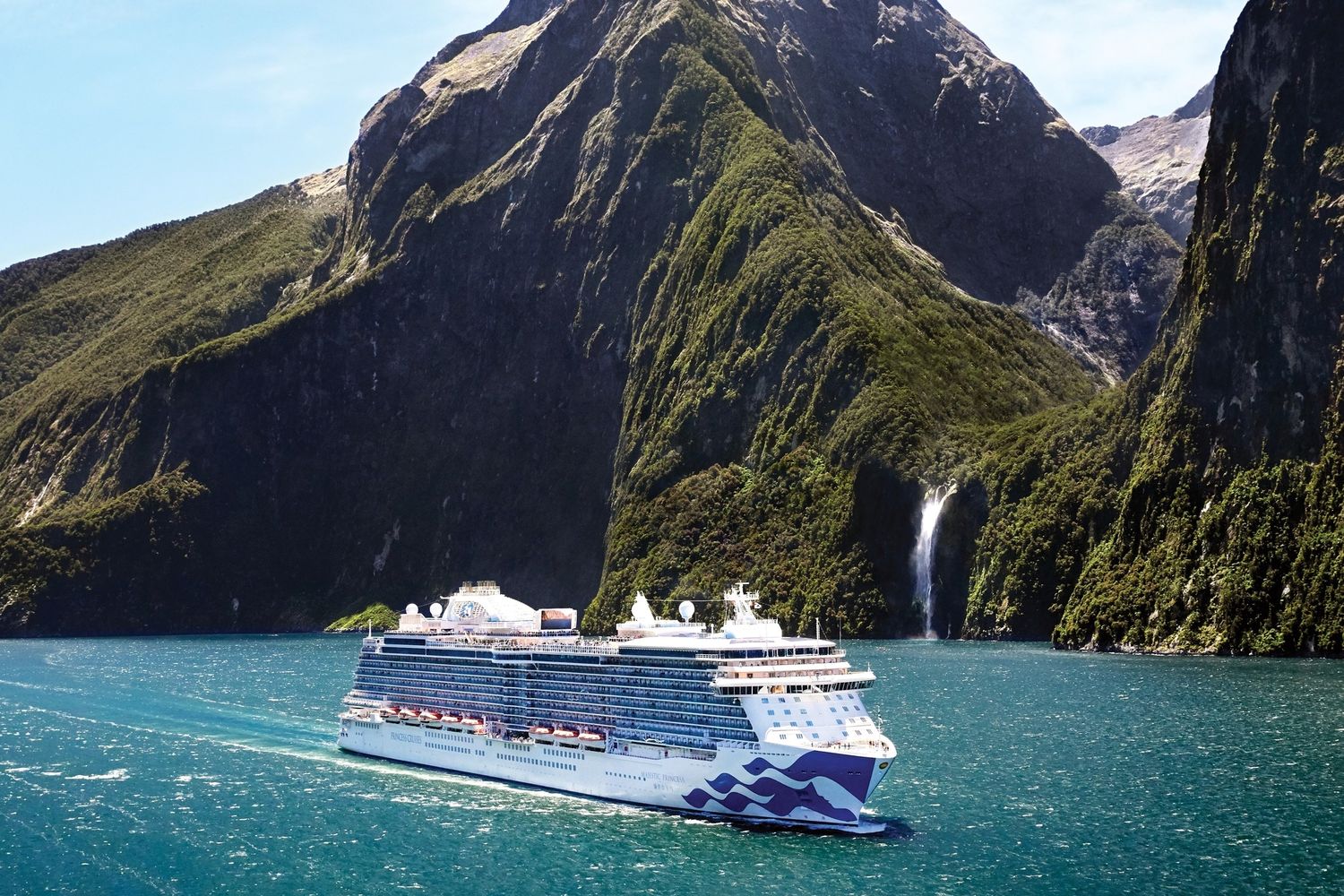 A cruise ship sails through the stunning turquoise waters of Milford Sound in New Zealand with towering cliffs and waterfalls.