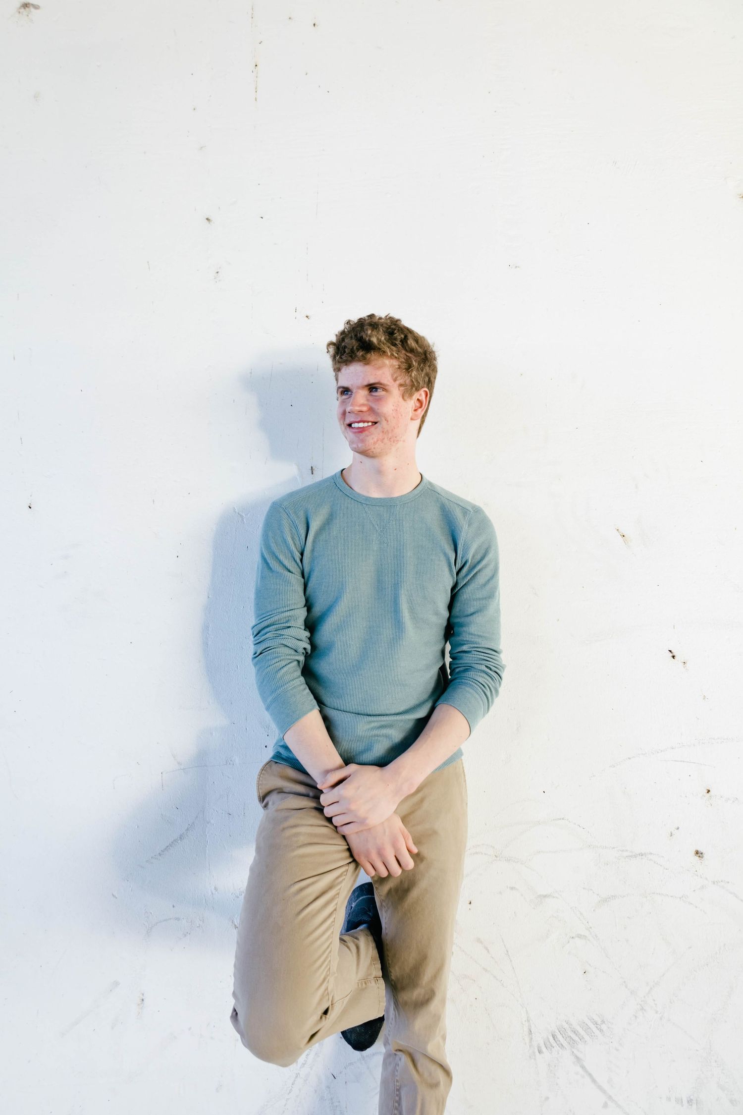 A casual portrait against a white wall shows someone wearing a blue sweater and khaki pants.