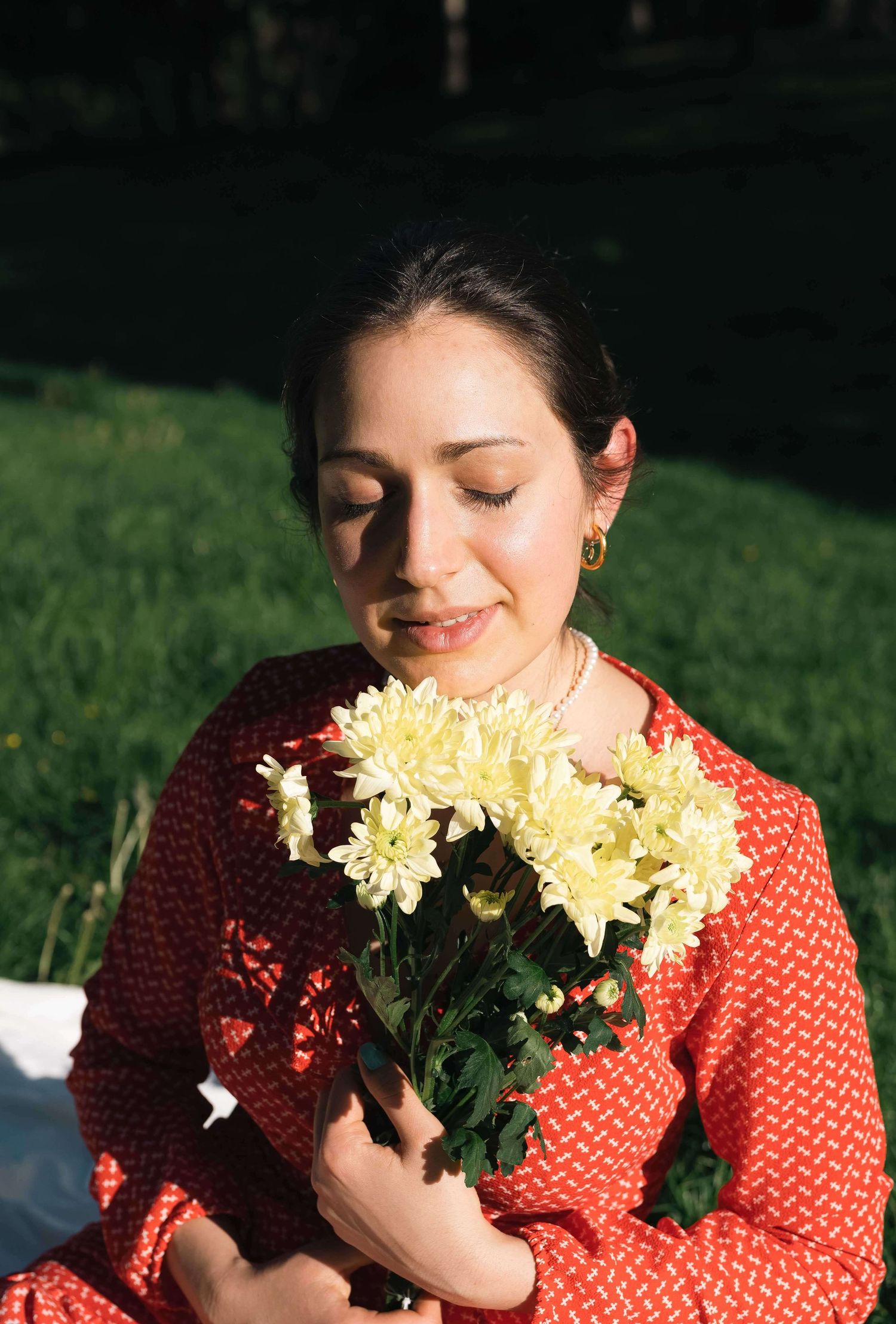 Person in red dress holding yellow chrysanthemums while basking in sunlight on grass.