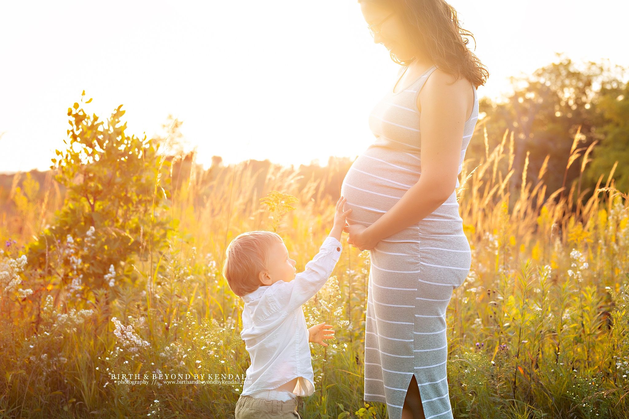 Silhouette of pregnant woman and child holding hands in golden sunlit field. Kendall Kuss Photography outdoor maternity photo in Waukesha WI