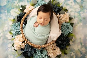 Sleeping newborn wrapped in mint green swaddle nestled in basket with blue and cream florals. Kendall Kuss Photography