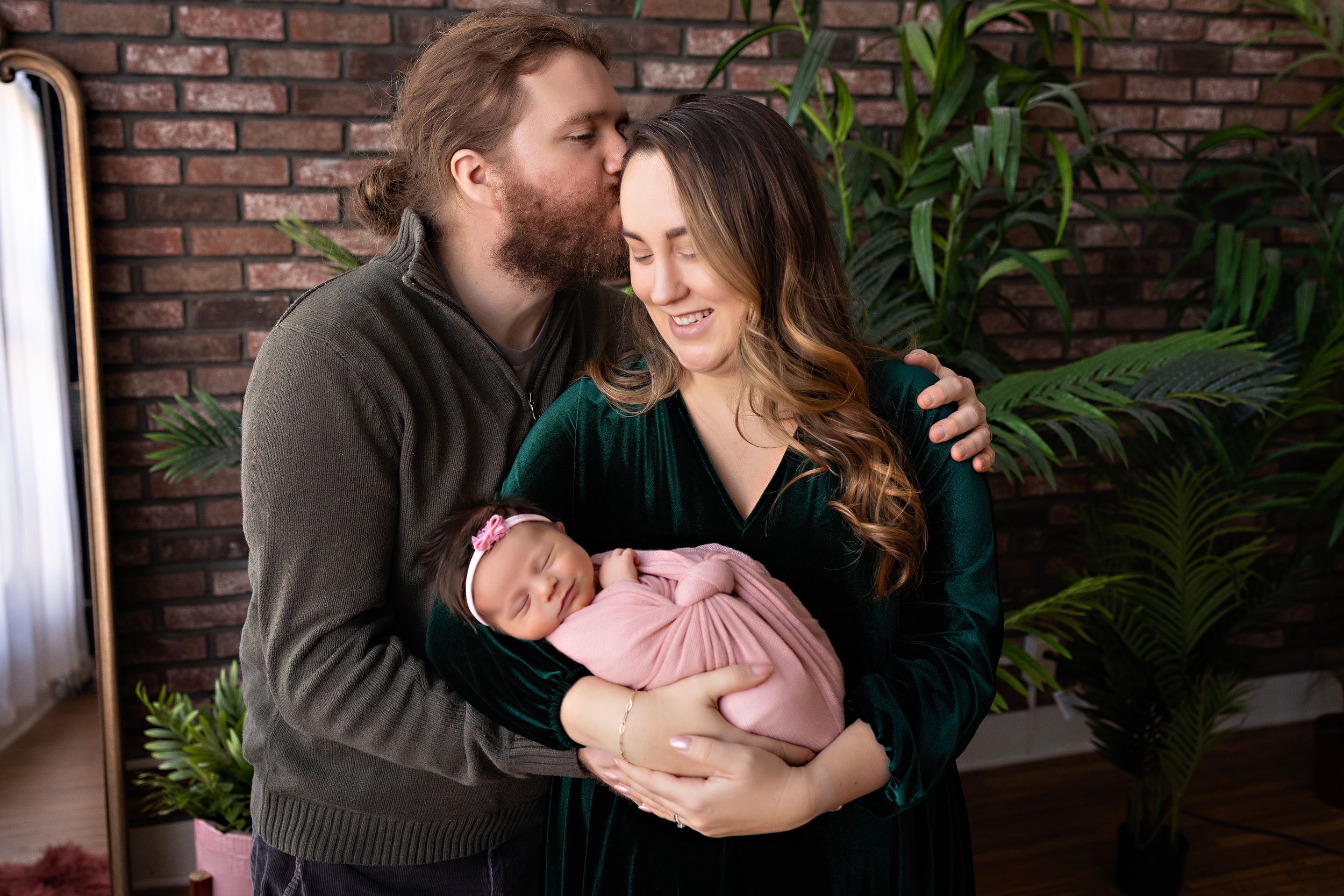 Family sharing intimate moment together while holding newborn against brick wall backdrop. Kendall Kuss Photography baby photos at studio