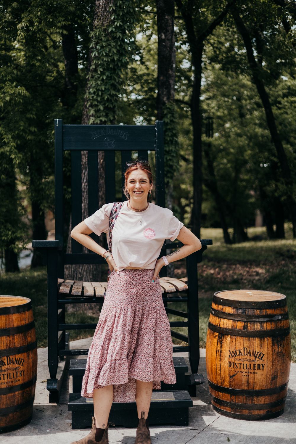 A rustic outdoor scene with a large black rocking chair and Jack Daniel's whiskey barrels in a wooded setting.