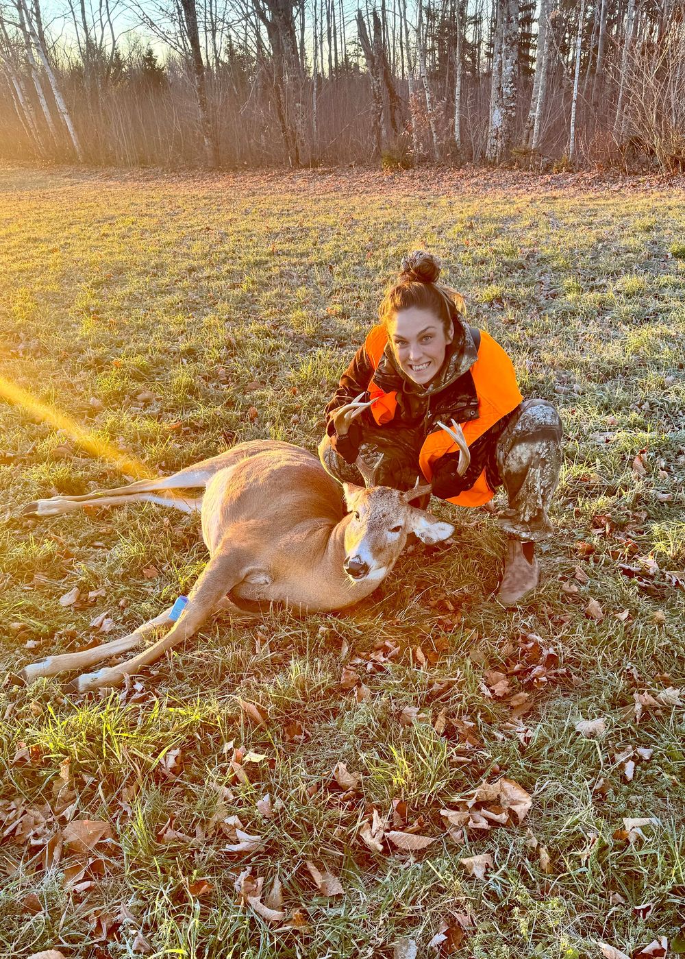 Person in orange jacket playing with a brown dog on grassy ground during golden hour sunset.