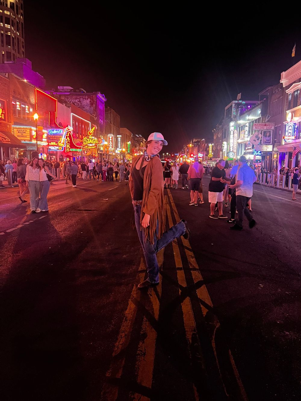 Nighttime street scene with colorful neon lights illuminating crowds of people walking along a busy entertainment district.