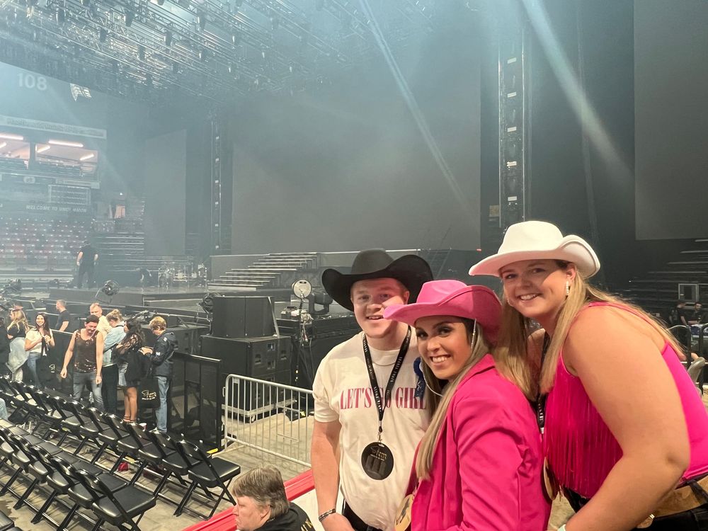 Concert attendees gather in an arena with folding chairs and atmospheric lighting creating a hazy ambiance.