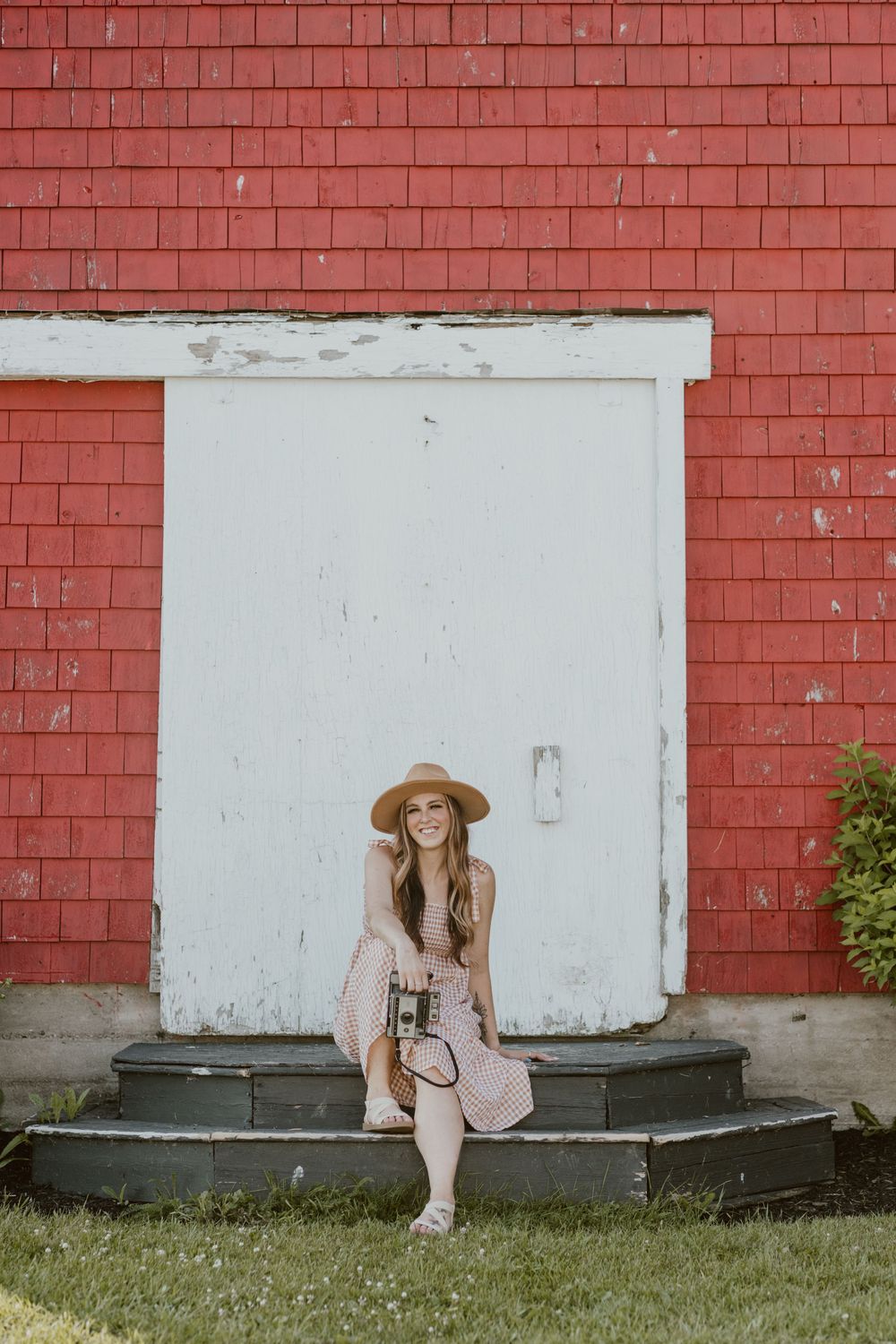 A white door on red brick wall with steps and grass in foreground creates rustic backdrop for outdoor portrait.