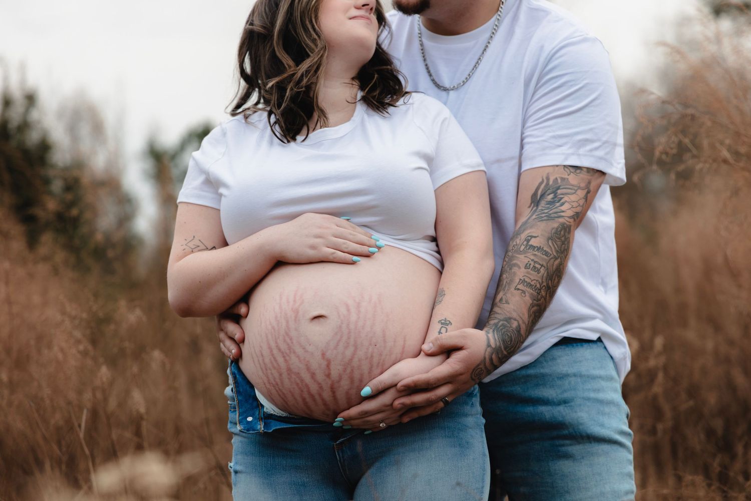 Maternity photo showing a pregnant belly with couple wearing white t-shirts outdoors.