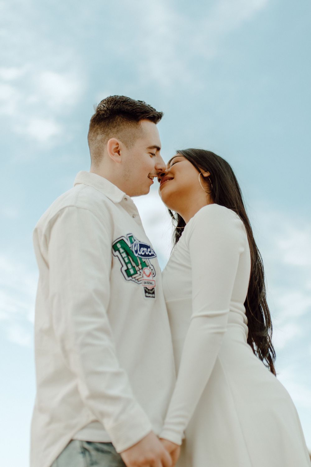 A tender moment captured against blue skies as a couple in white outfits share an intimate moment.