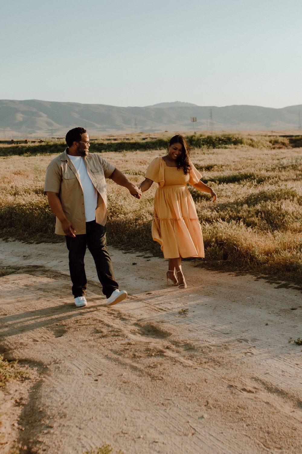 Couple enjoying a sunset walk together on a dirt path with mountains in the background.