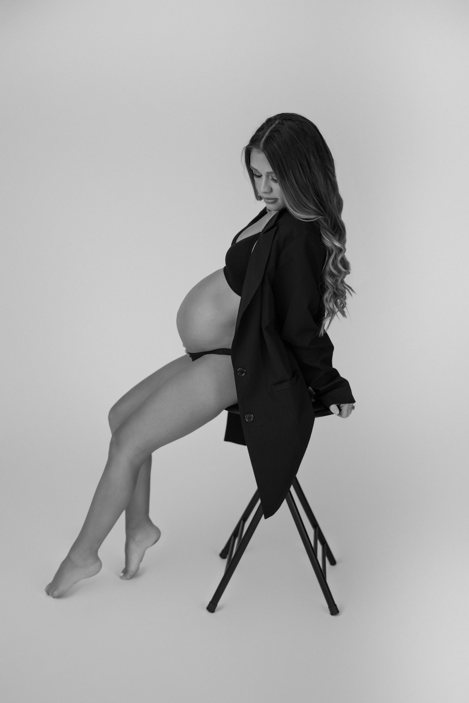 Artistic black and white maternity portrait on stool shows elegant pose.