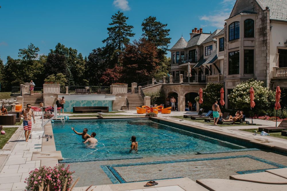 Guests swimming and relaxing at a stunning luxury estate pool on a sunny day.