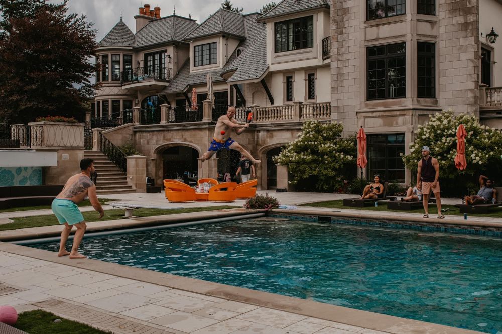 People enjoying a summer pool party at a large luxury estate with an orange inflatable.