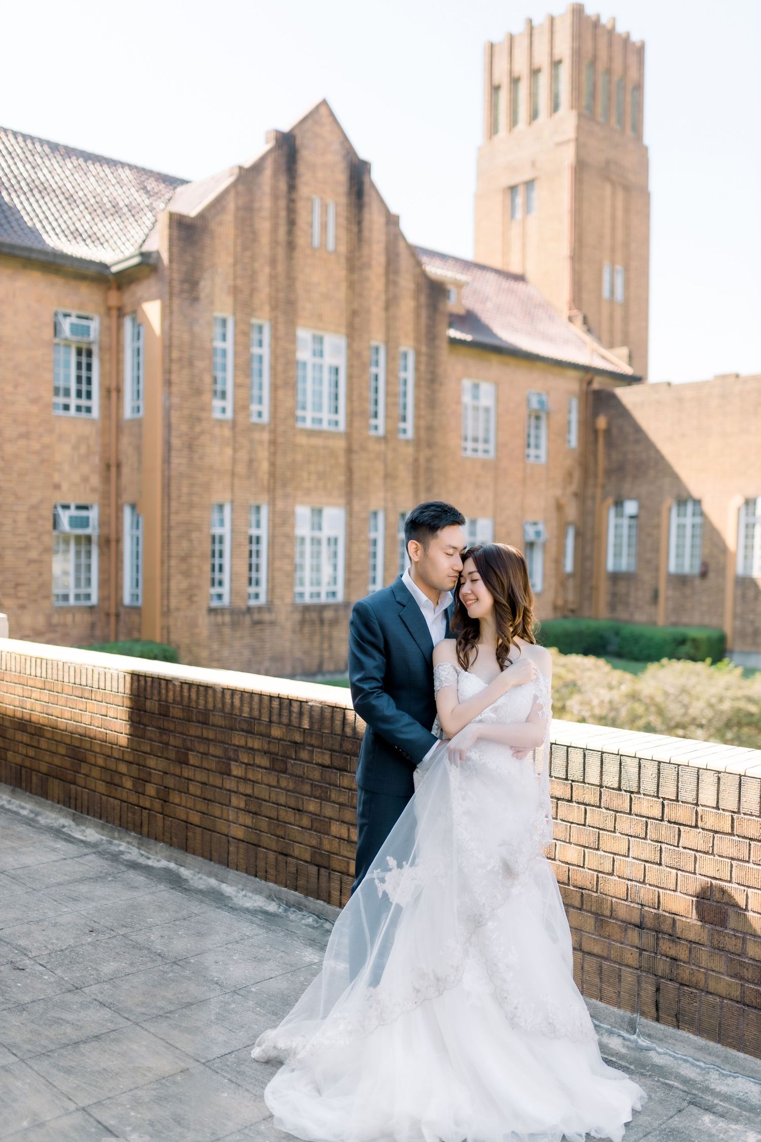 Wedding couple posing against brick building with Gothic architecture.
