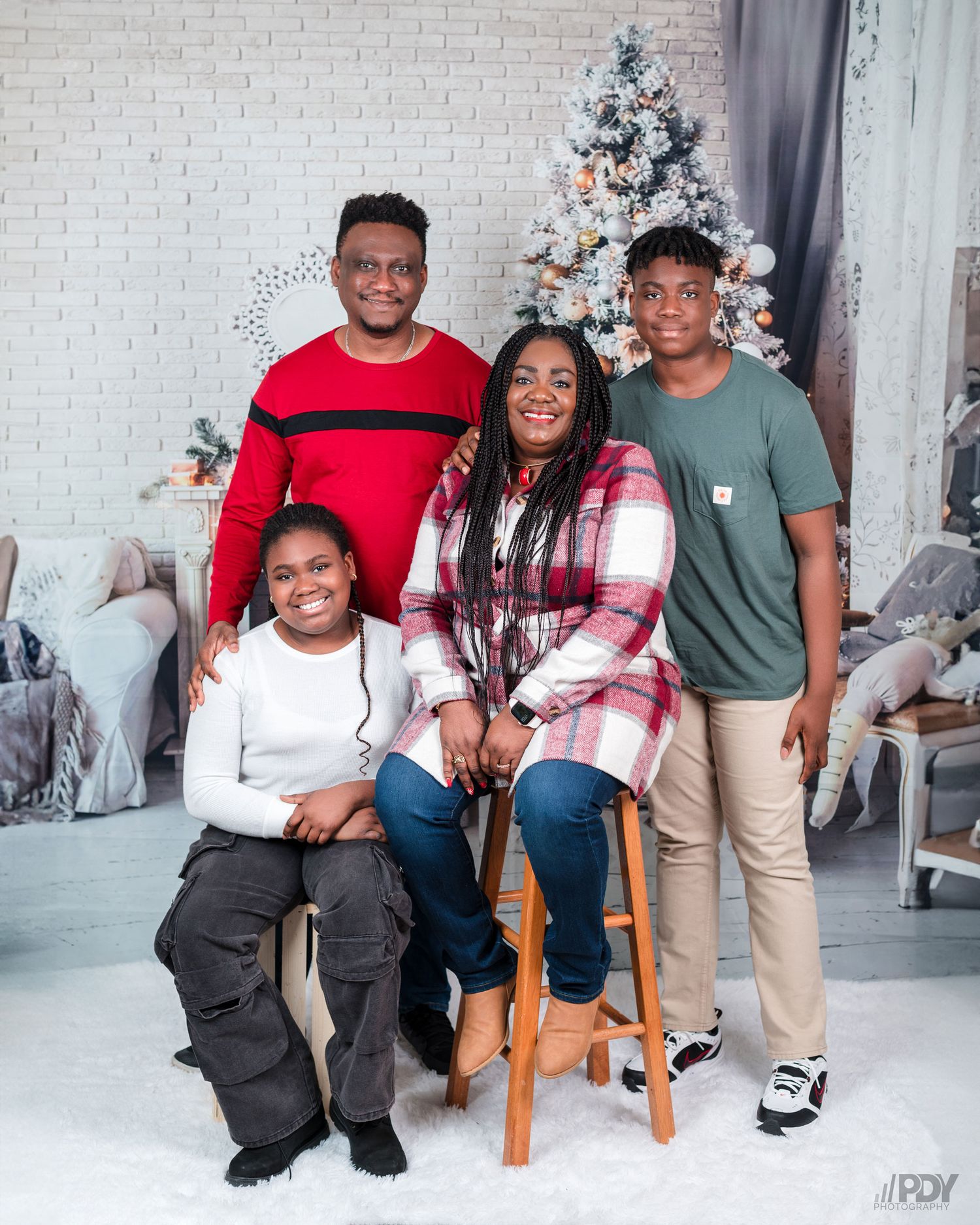 Family group photo session in casual attire against white brick wall with Christmas decor.