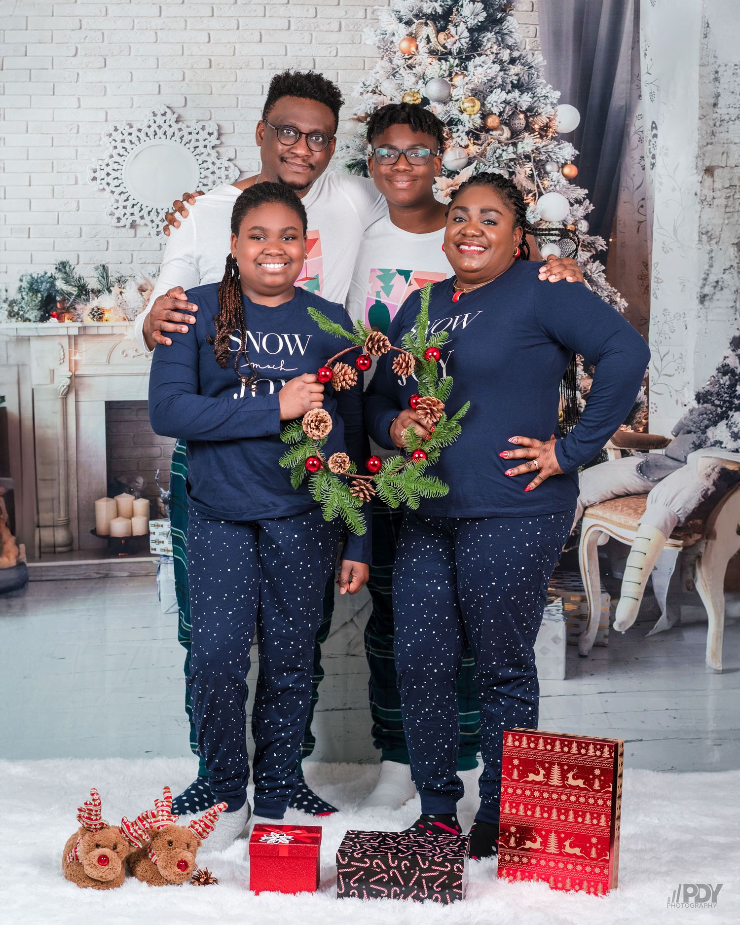 Family wearing matching navy outfits poses by Christmas tree with wrapped presents.