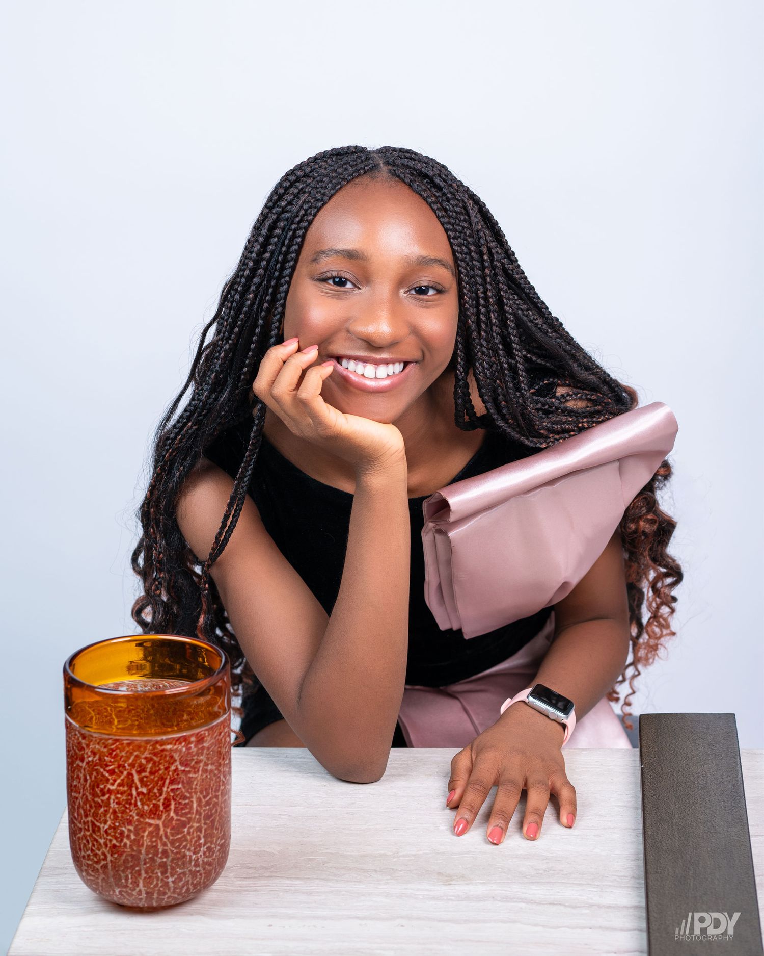 Portrait featuring bright smile and beverage on white desk with soft pink accents.