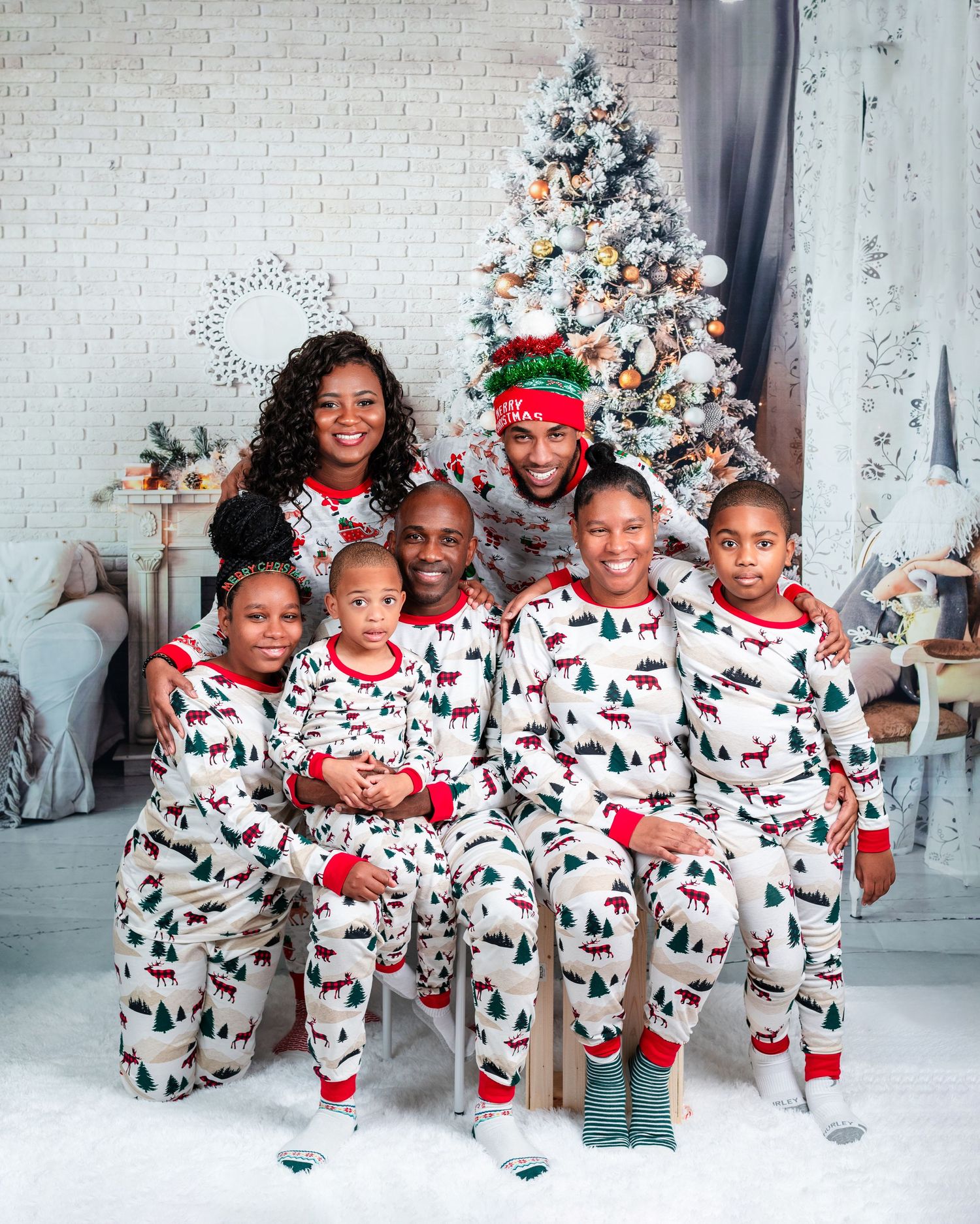 Family group wearing matching Christmas pajamas pose together by decorated white tree.