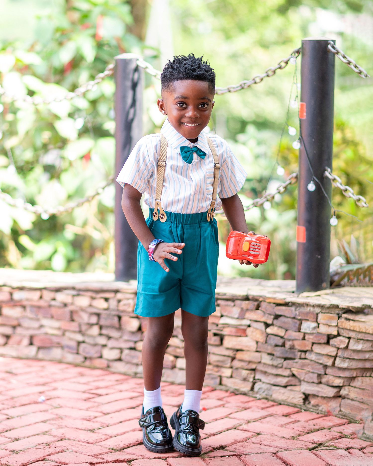 Child wearing teal shorts and bow tie outfit posing on brick walkway.