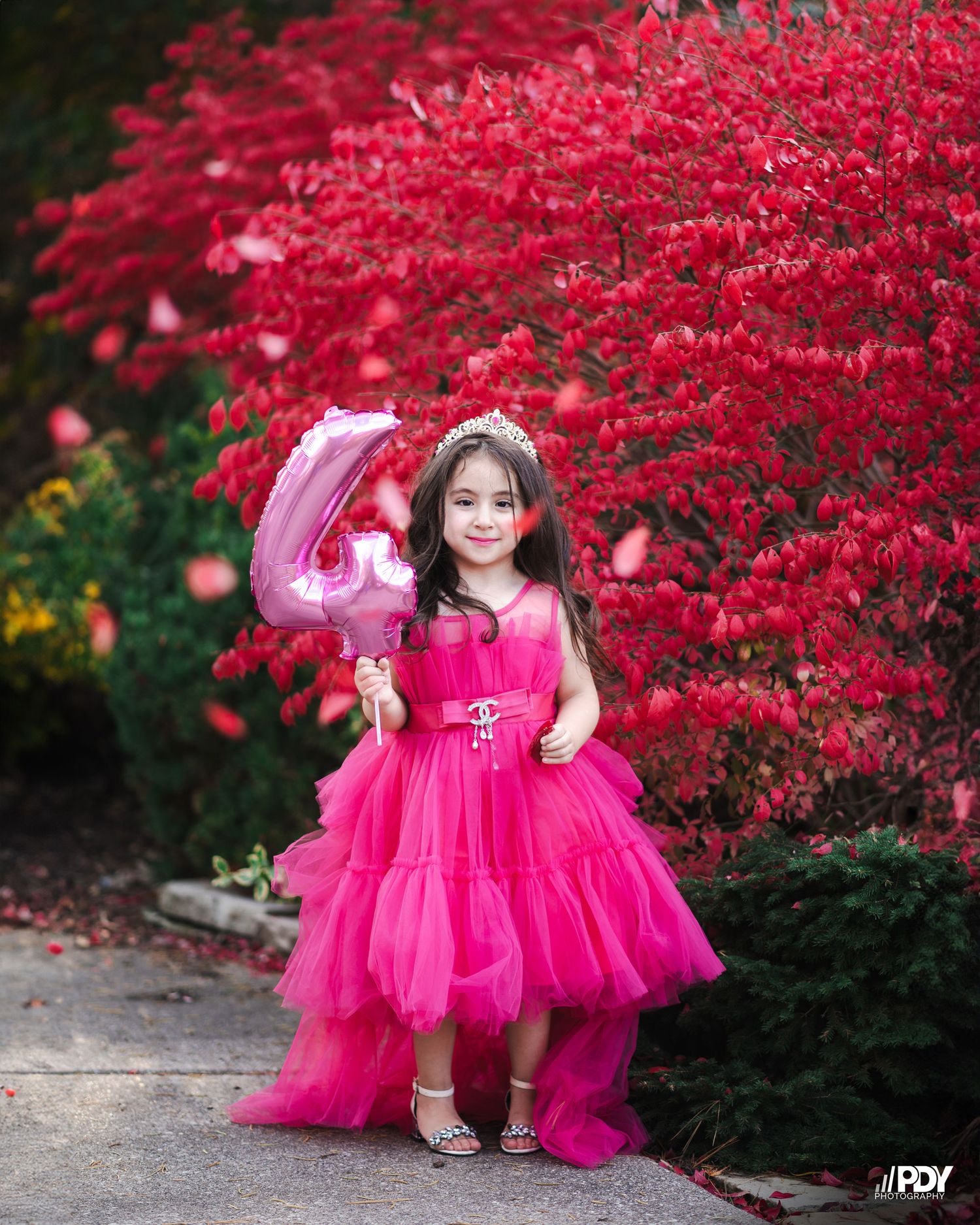 Bright pink tulle dress twirls against vibrant red autumn foliage backdrop.