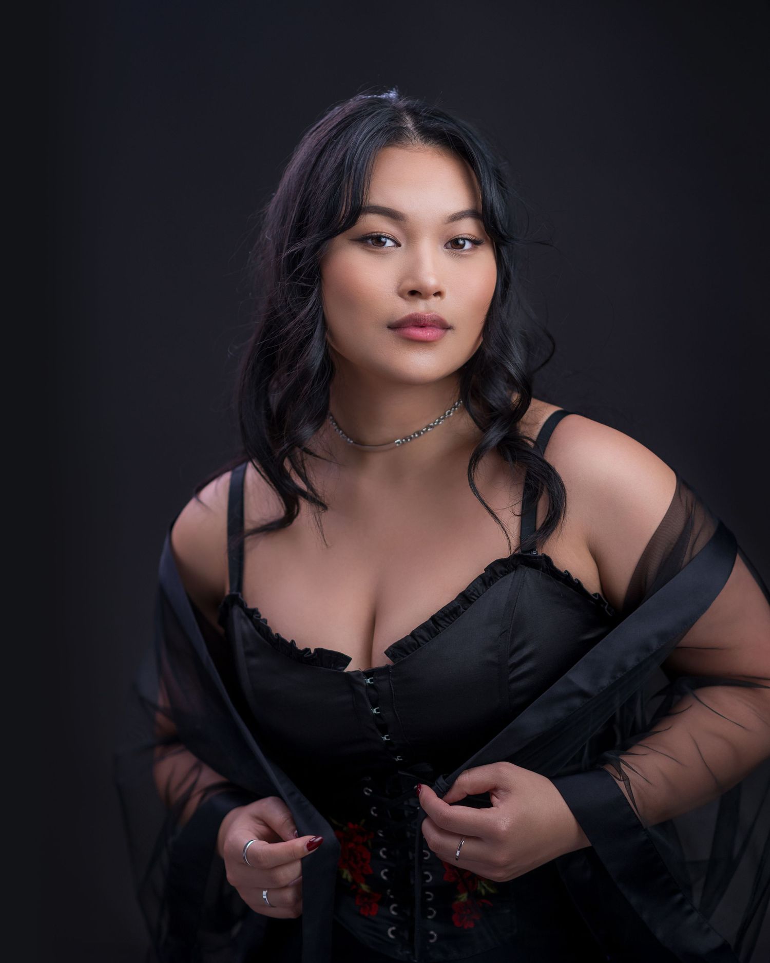A dramatic boudoir portrait against black background featuring elegant black attire.