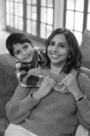 Black and white portrait of a smiling mother and young son embracing on a couch together.
